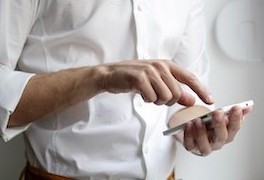 Torso of man in white button-up shirt tapping a smart phone